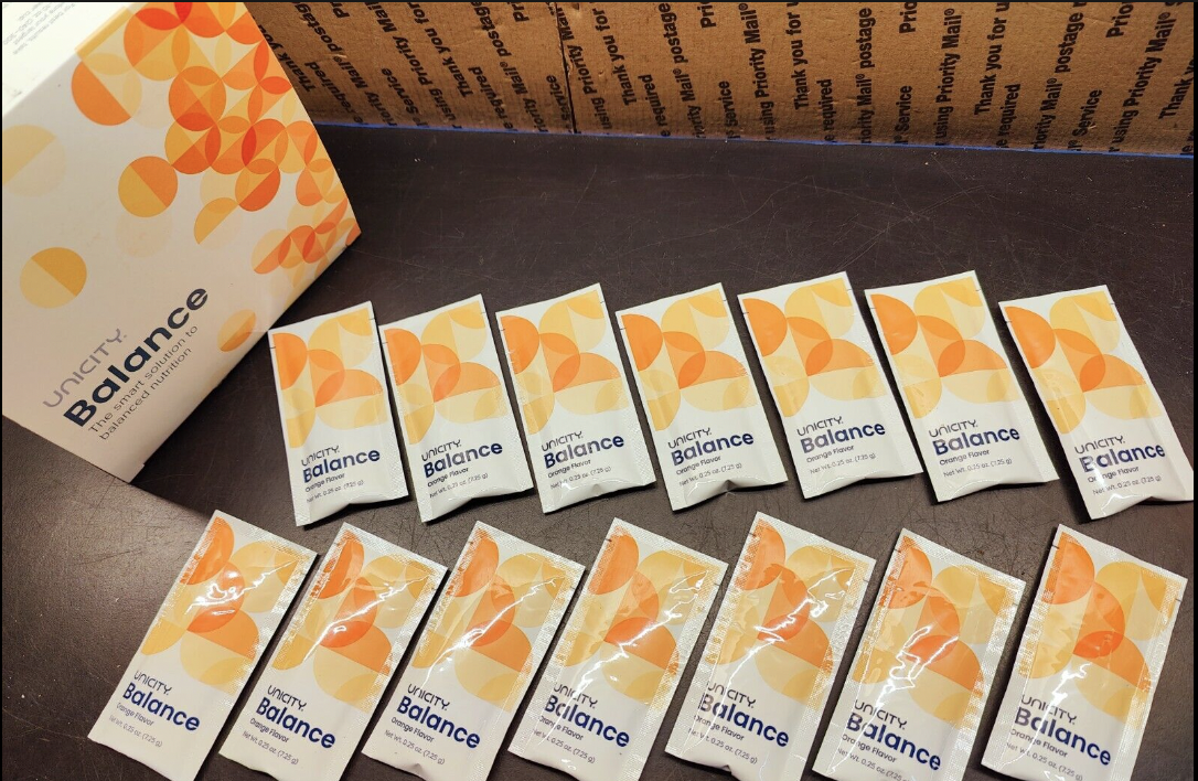 14 Unicity balance packets lined up on a table beside the box it comes in. 