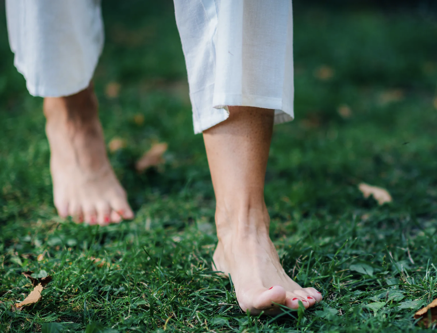 An up close picture of a woman's feet as she walks barefoot in the grass to achieve the beneficial effects of grounding. 